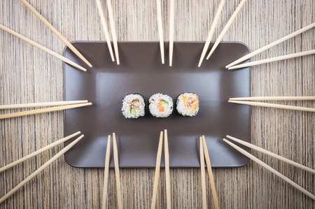 Three sushi roll in a plate with a many of chopsticks on a wooden dark table.の写真素材