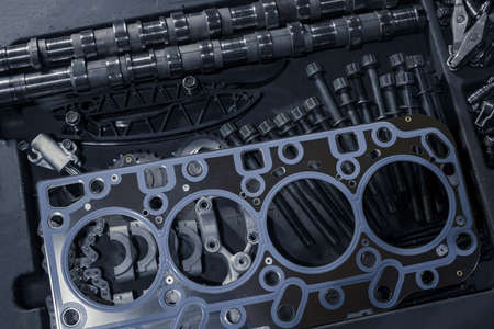 A new cylinder head gasket with various timing parts on a table in a car repair shop. Repair of an old diesel engine. Bolts camshafts, gear chains and timing tensioners before installation on a car.の写真素材