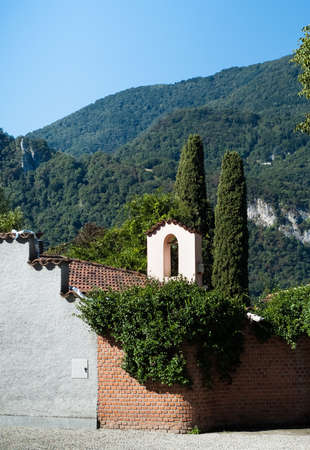 a small bell tower photographed against cypress trees and mountains in Abbadia Lariana, Italyの写真素材