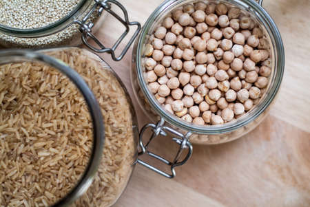 closeup photo of glass jars with brown rice, chickpeas, and quinoaの写真素材