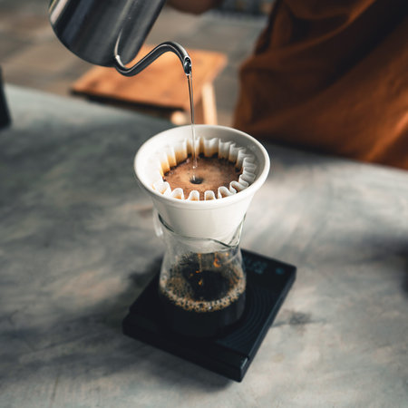 Drip coffee, barista pouring water on coffee ground with filter at home