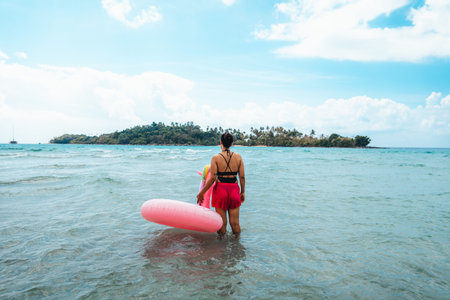 A woman walks into the clear sea on Koh Phrao. Rubber rings for playing in the water in summer