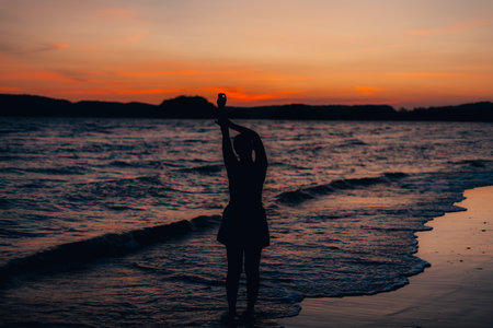 silhouette of woman at beach at dusk,Woman raising her hand on the beach at duskの写真素材