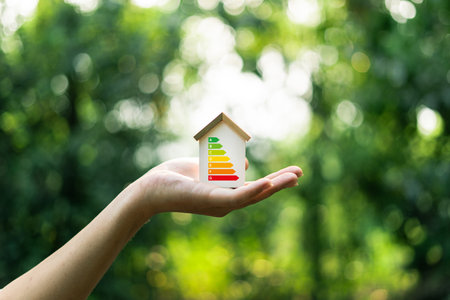 Home Energy Efficiency, Eco-Friendly Home Improvement,Wooden toy house in hand on natural green eco backgroundの写真素材