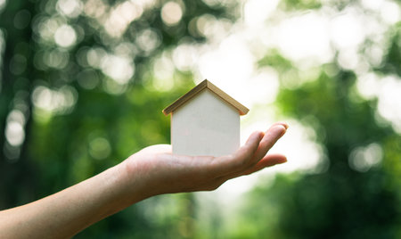 Eco-friendly house concept, wooden house decoration on hand green natural backgroundの写真素材