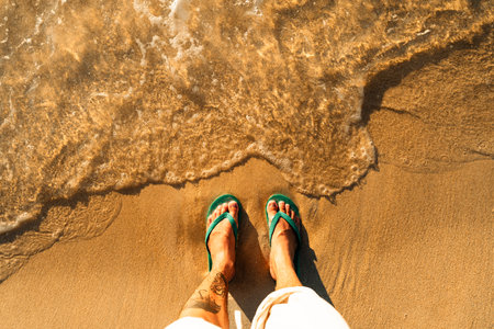 green flip-flops resting on golden sand, with footprints indicating a leisurely summer stroll along the beachの写真素材