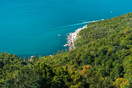 An exquisite aerial view of Bottle Beach, embraced by lush green forests, with vibrant turquoise waters contrasting against the azure sky on a summer day in Koh Phangan, Thailand.の写真素材