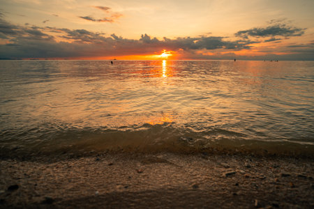 sun setting low over the ocean water on a summer evening. Orange and golden light glimmers brilliantly on the water's surface and the horizonの写真素材