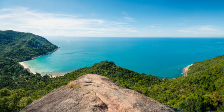 An exquisite aerial view of Bottle Beach, embraced by lush green forests, with vibrant turquoise waters contrasting against the azure sky on a summer day in Koh Phangan, Thailand.の写真素材