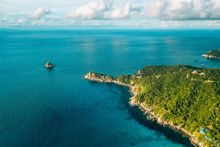 aerial perspective captures the dramatic meeting point of a lush, verdant tropical island and the vast, deep blue ocean.の写真素材