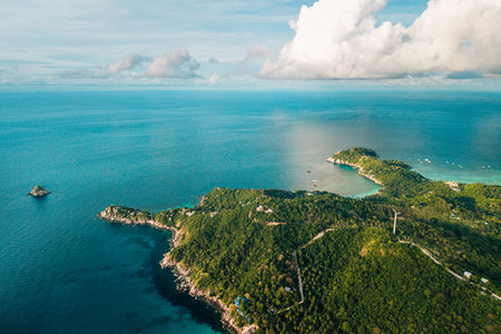 aerial perspective captures the dramatic meeting point of a lush, verdant tropical island and the vast, deep blue ocean.の写真素材