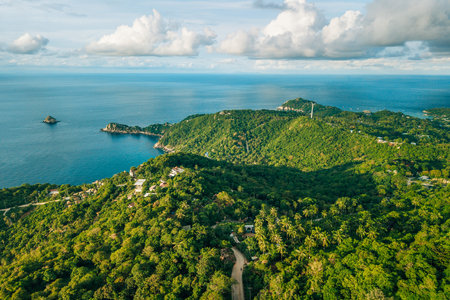 aerial perspective captures the dramatic meeting point of a lush, verdant tropical island and the vast, deep blue ocean.の写真素材