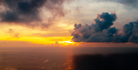 A breathtaking photograph of the sun nearing the horizon over a vast ocean. A striking golden-orange beam of light extends across the water's surfaceの写真素材