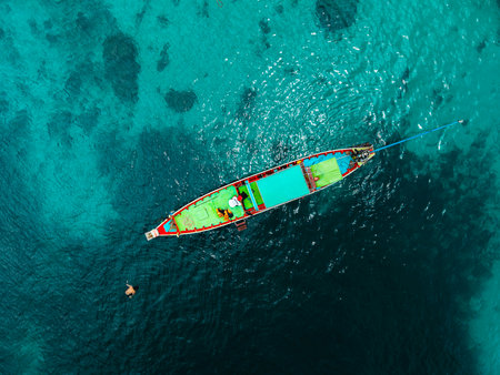 erial view captures the essence of a tropical paradise. A traditional colorful Thai longtail boat with a person standing on it floats gracefully on the crystal-clear turquoise waters.の写真素材