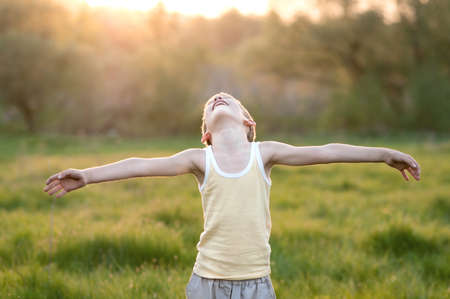 Boy stands in a green meadow at sunsetの写真素材