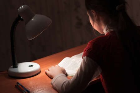 the girl at the desk reading a book by the light of the lampの写真素材