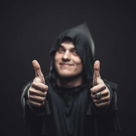 Smiling guy in a black robe showing thumbs upの写真素材