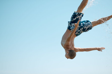 young guy in shorts coming down against the sky in a spray of water