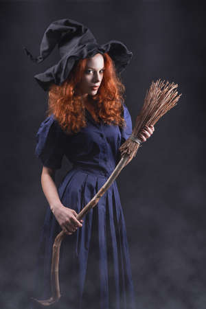 Young beautiful red-haired witch with a broom in the dark fogの写真素材