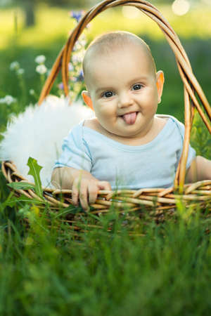 small smiling child in sliders showing tongue, sitting a basket on the grassの写真素材