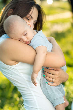 Happy mother holding a young sleeping son in the parkの写真素材