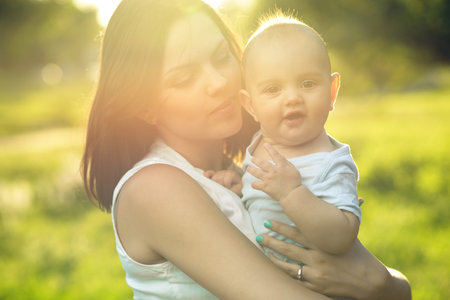 Happy mother holding a young son in the park sunlight