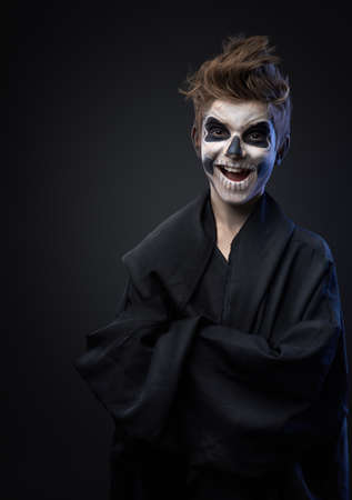 Teen with make-up of the skull in a black cloak laughsの写真素材