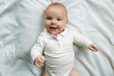 cheerful smiling baby lying on a white rugの写真素材