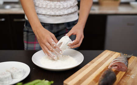 girl roll slice of  fish in flour in the kitchenの写真素材