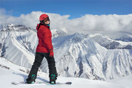 snowboarder in a red jacket on the edge of a cliff. She turns around smiling.の写真素材