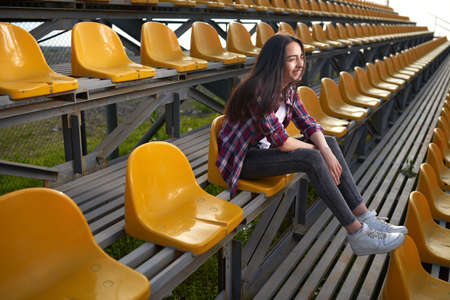 beautiful lonely woman sitting on tribunes and laughs. Side view.の写真素材