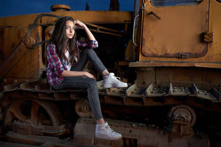 beautiful teen girl sitting on an old tractor tracks.の写真素材