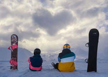 Clouds in the shape of heart, Male and female snowboarders sitting and smiling with winter landscape.の写真素材