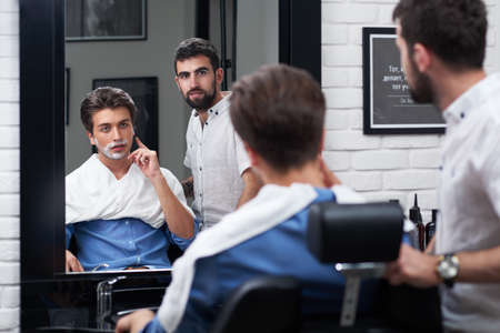 The client and barber look in the mirror and choose the design of the beardの写真素材