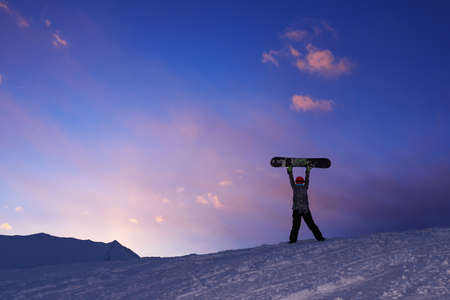 Girl raises snowboard up against the dark sunset skyの写真素材