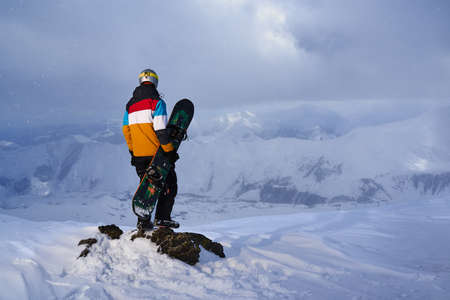 Snowboarder standing on a rock on the edge of a cliff and looking down.の写真素材