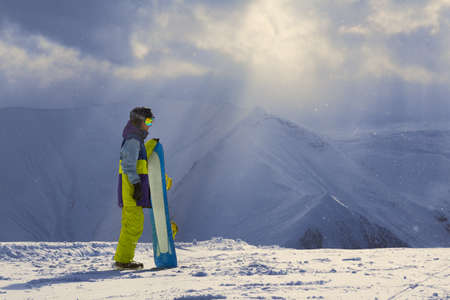 Snowy weather in the mountains snowboarder stands sideways on the edge of a cliff.の写真素材