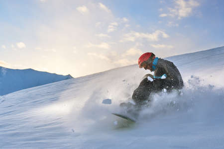 Girl snowboarder slows down the slope on a background of sunset sky, snow splashesの写真素材