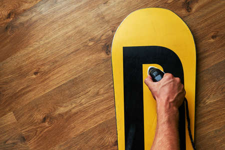 man ironed wax on a snowboard, lying on the wooden floorの写真素材