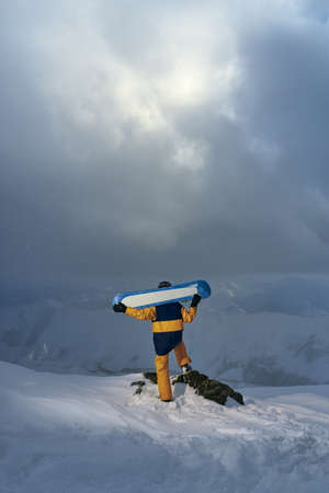 snowboarder stands on a cliff and holding the board on their shoulders in the winter in the mountainsの写真素材