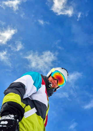 a man in a ski suit standing and looking into the camera view from belowの写真素材