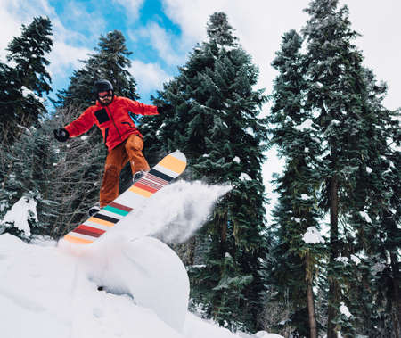 snowboarder with special equipment is jumping very high and freeriding from snowdrift, hill in the mountain forestの写真素材