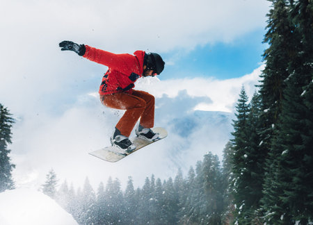 snowboarder in red suit is riding fast and jumping high in the mountain forestの写真素材