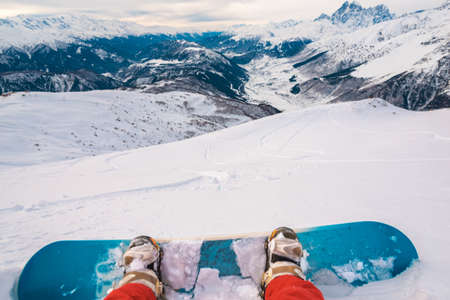snowboarder with snowboard is sitting on the mountain and watching the beautiful mountain viewの写真素材