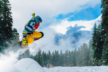 snowboarder in red suit is riding fast and jumping high in the mountain forestの写真素材