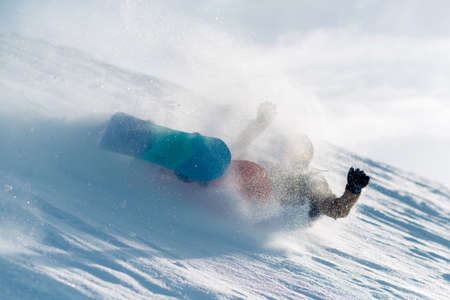 snowboarder is riding with snowboard from powder snow hill very fast and fall downの写真素材