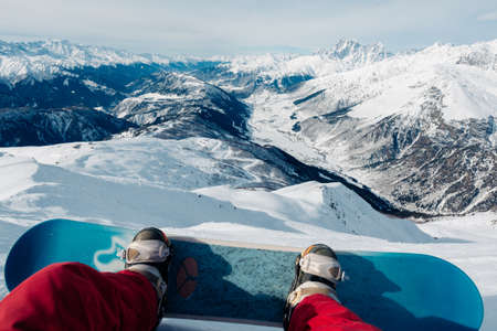 snowboarder with snowboard is sitting on the mountain and watching the beautiful mountain viewの写真素材