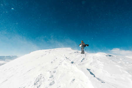 snowboarder is standing on the snow hill with snowboard and watchingの写真素材