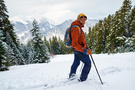 man skier in gear stands on a slope in the forest against the backdrop of mountains