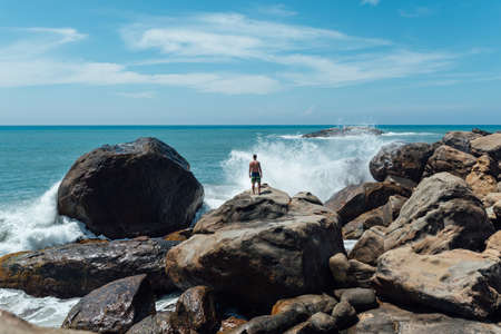 man stands on a rock and looks at the ocean, waves of waves fly upwardの写真素材